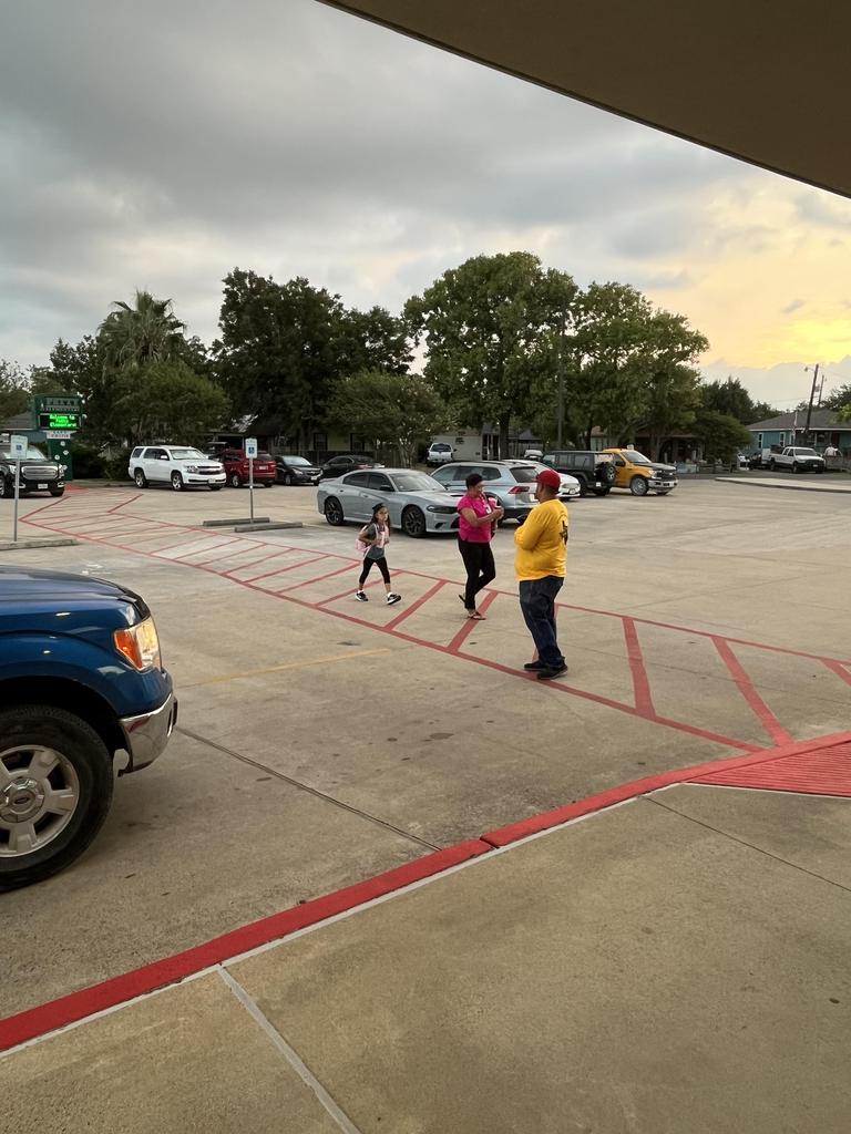 A group of people walking through a parking lot, with various cars parked in the background.