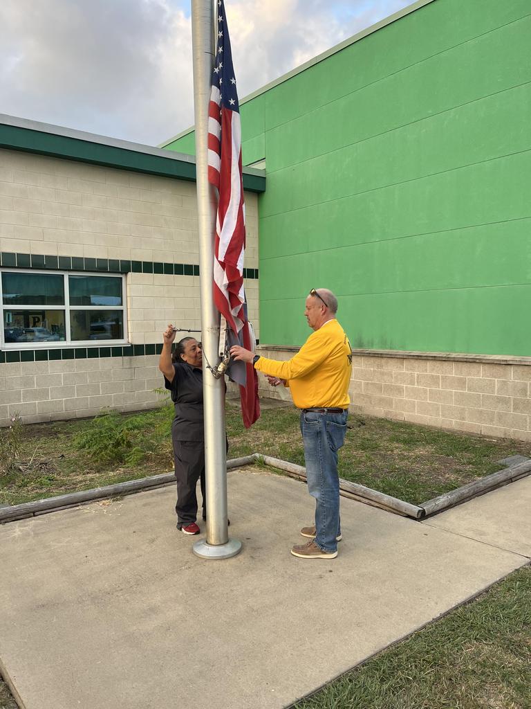 Two individuals stand beside a flagpole, showcasing a moment of camaraderie and patriotism in a public space.