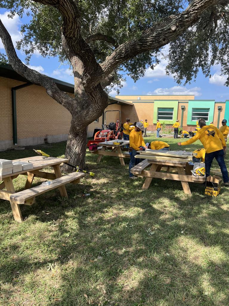 Two men in yellow shirts collaborate on a picnic table, engaged in a productive outdoor activity.