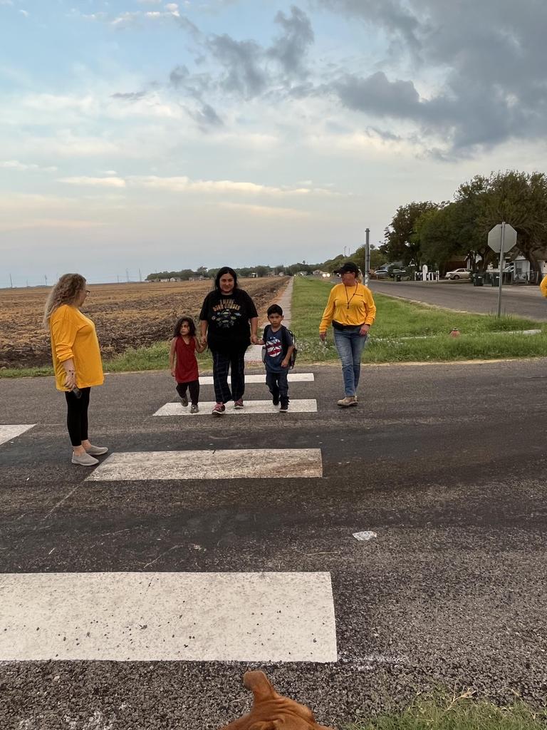 A diverse group of individuals crossing the street, with a dog observing them from the sidewalk.