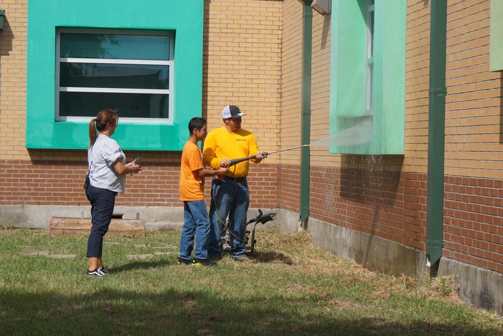 Two individuals and a child are using a hose to spray water on a wall, engaging in a fun outdoor activity.