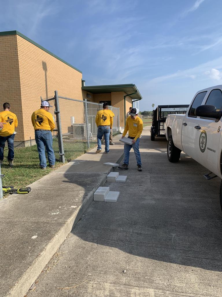 A group of individuals in yellow shirts collaborates on a sidewalk project, demonstrating teamwork and community engagement.