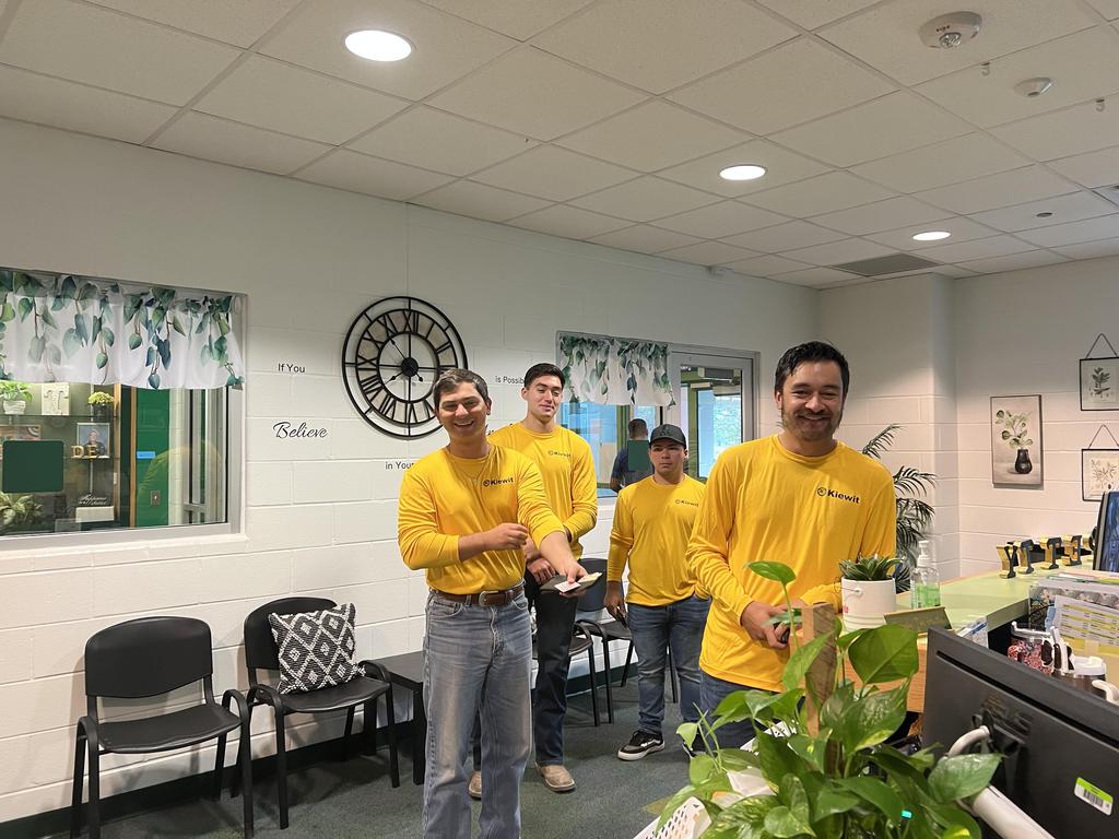 A group of individuals wearing yellow shirts gathered in front of a desk, engaged in conversation or activity.