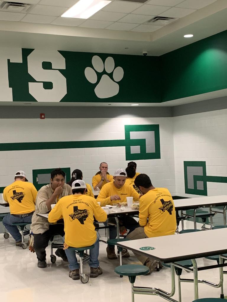 A diverse group of individuals seated at tables, engaging in conversation in a bustling cafeteria setting.
