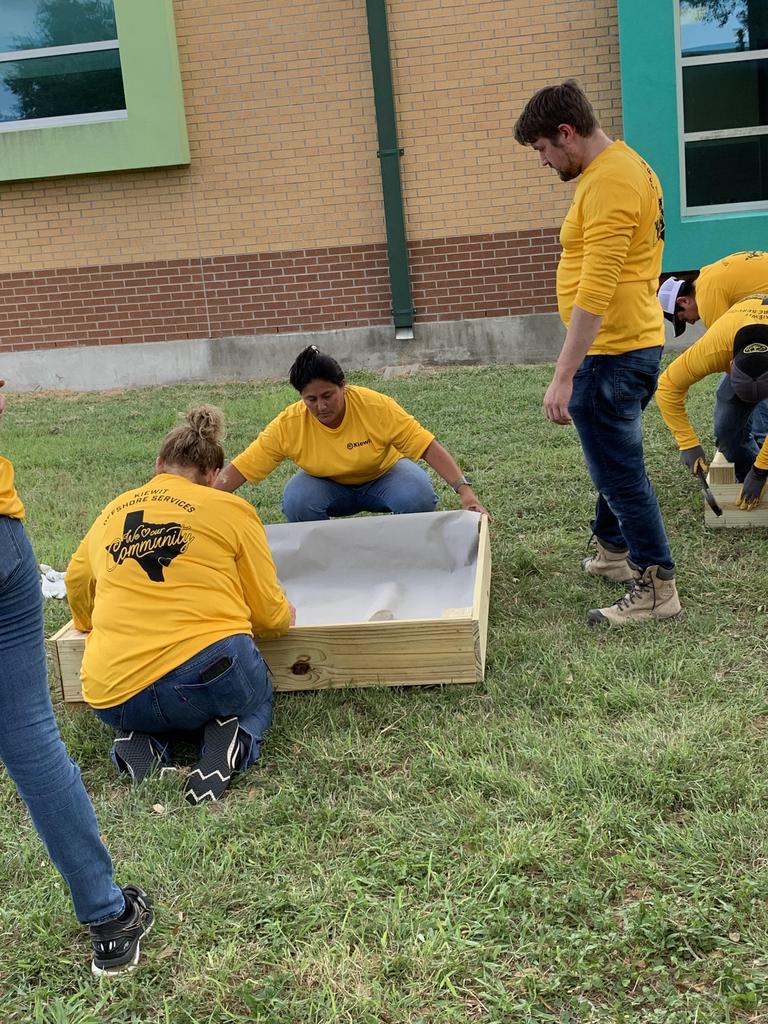 A group of individuals in yellow shirts collaboratively working on a large box, demonstrating teamwork and focus.