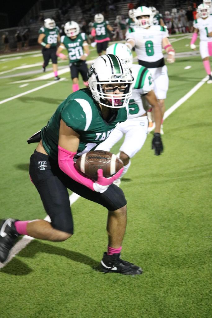 A football player sprinting down the field, skillfully carrying the ball towards the goal line.