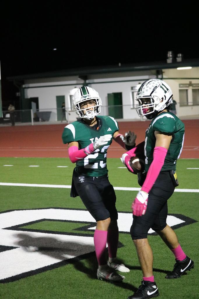 Two football players in green and pink uniforms compete on the field, showcasing athleticism and teamwork.