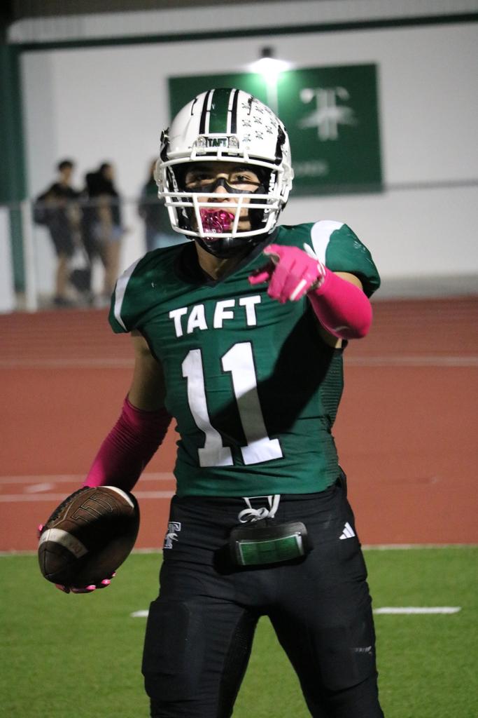 A football player in a green uniform stands confidently, holding a ball in preparation for the game.
