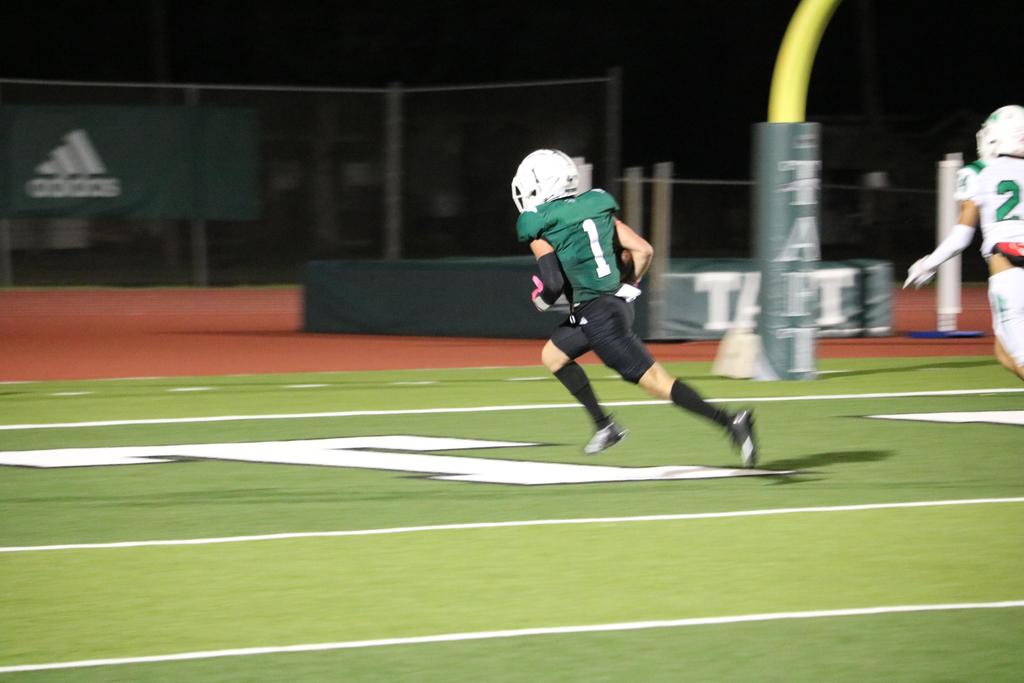 A football player sprinting across the field under the night sky, illuminated by stadium lights.