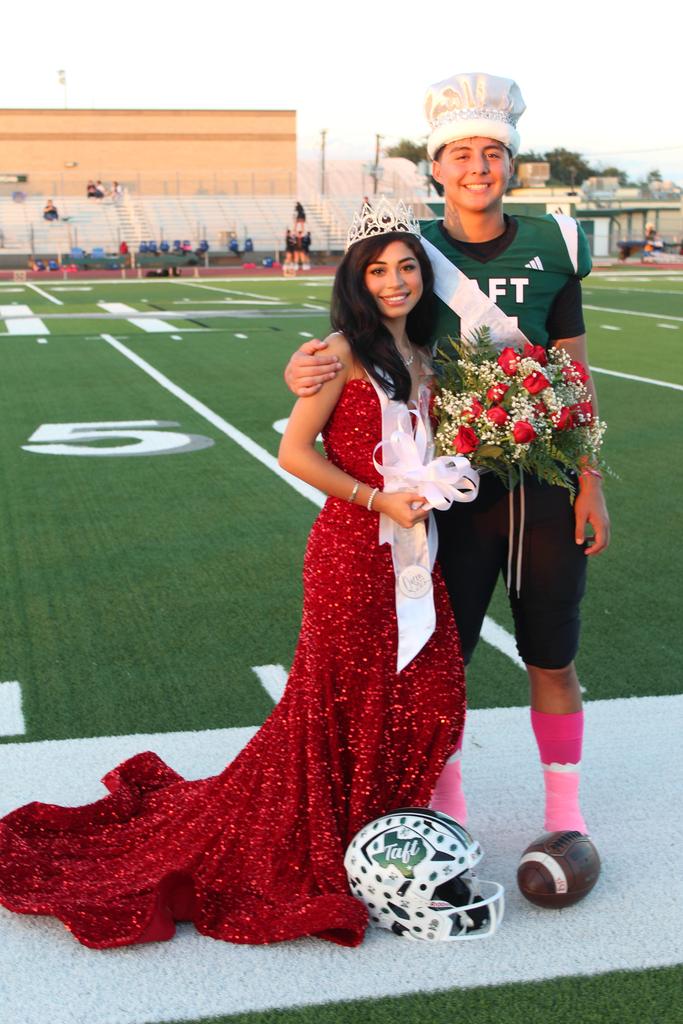 A man and woman in red dresses pose together on a vibrant football field, showcasing a striking contrast with the green grass.