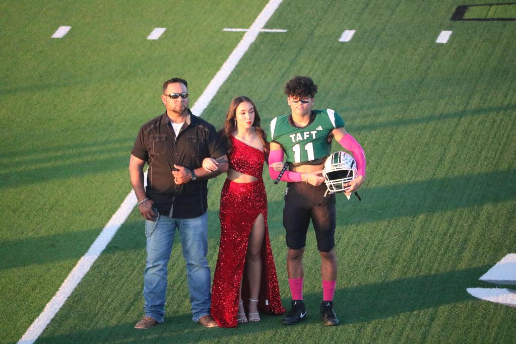 Two individuals and a woman in a red dress pose together on a football field, showcasing a vibrant outdoor scene.