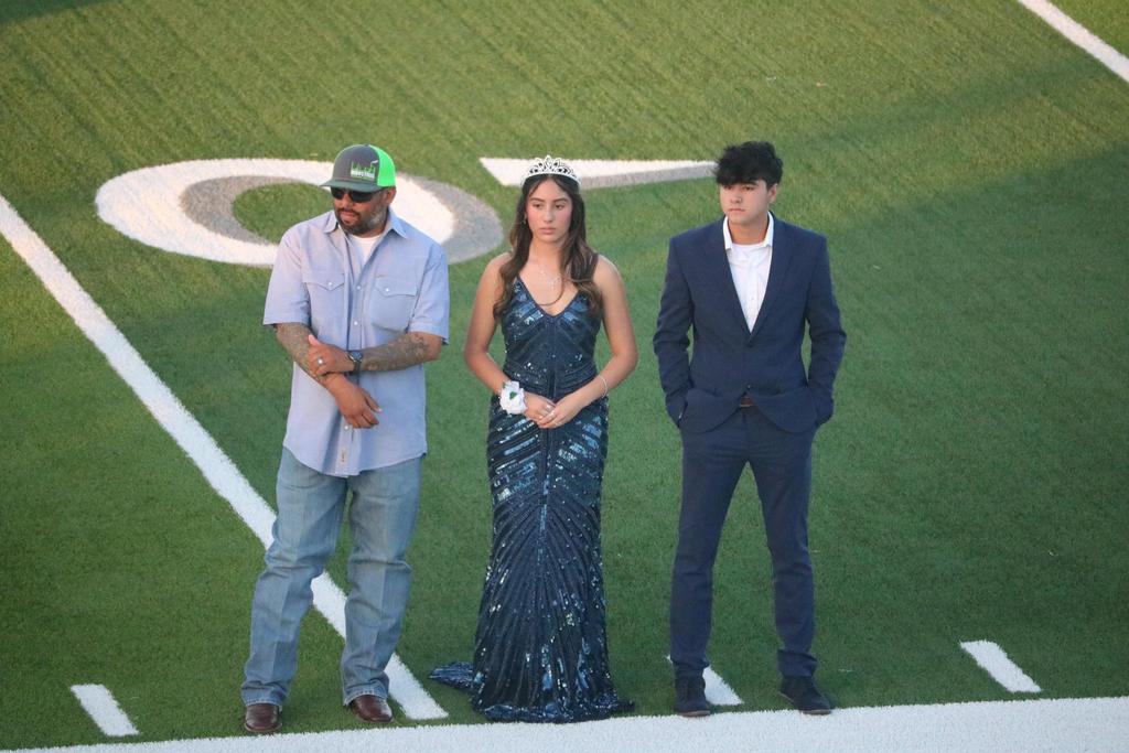 Three individuals in formal attire pose together on a football field, showcasing a blend of elegance and athleticism.