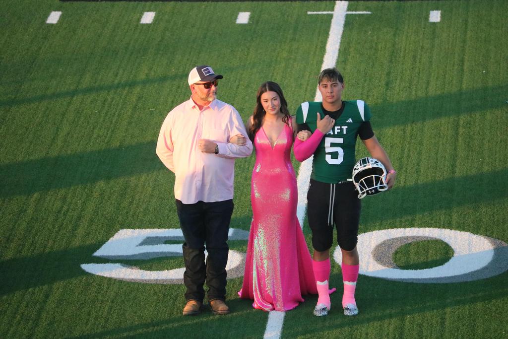 Two individuals in pink dresses pose together on a football field, showcasing a vibrant and lively atmosphere.