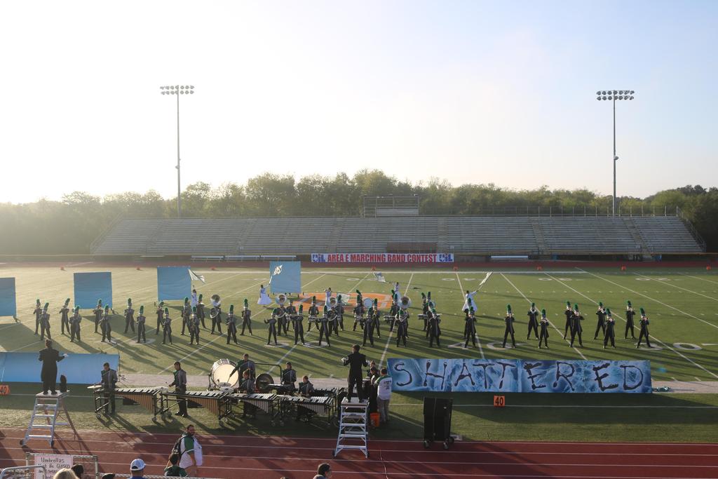 A band performs on a football field, accompanied by a colorful banner displaying their name and logo.