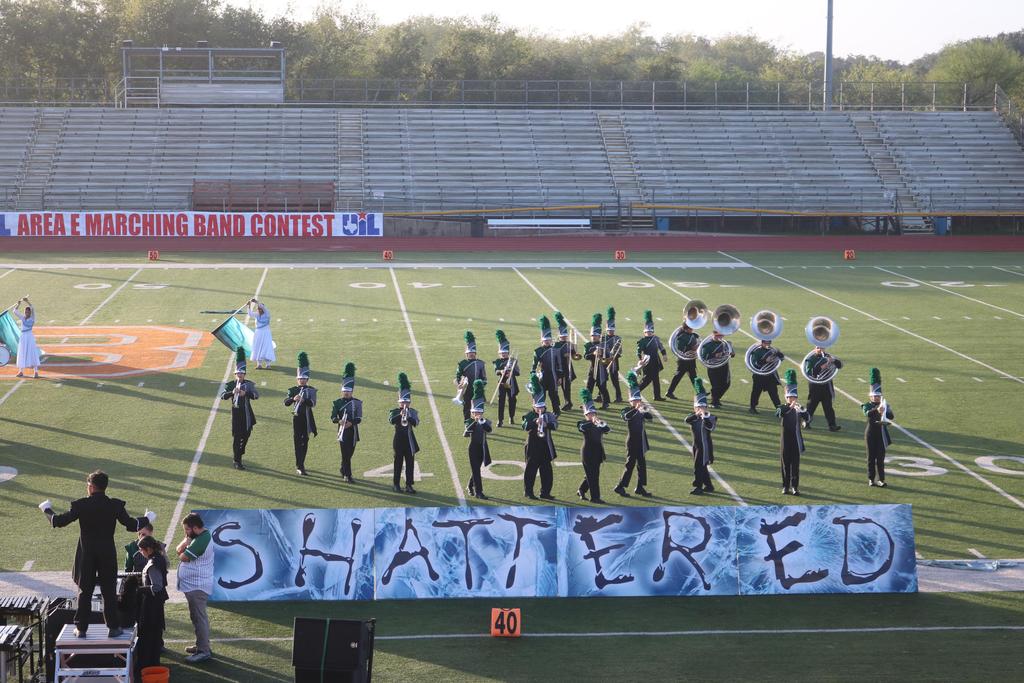 A band performs on a football field, with a prominent banner displaying the word "shattered" in the background.
