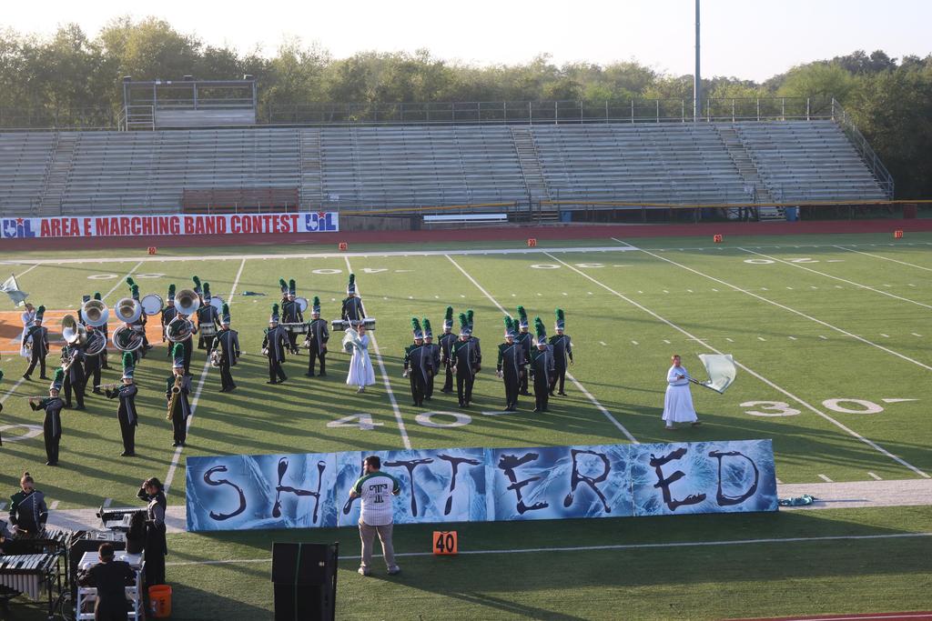 A band performs on a football field, accompanied by a banner displaying the word "shattered."