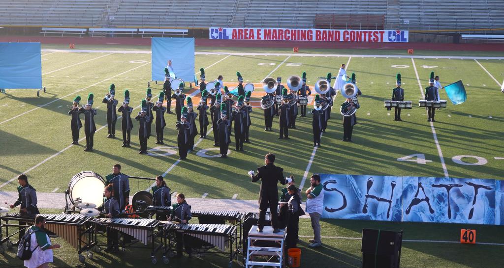 A band performs on a football field, accompanied by a colorful banner displaying their name and logo.