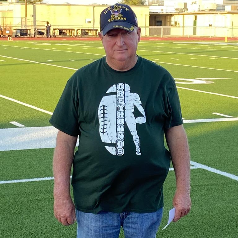 A man wearing a green t-shirt stands confidently on a football field, ready for action.