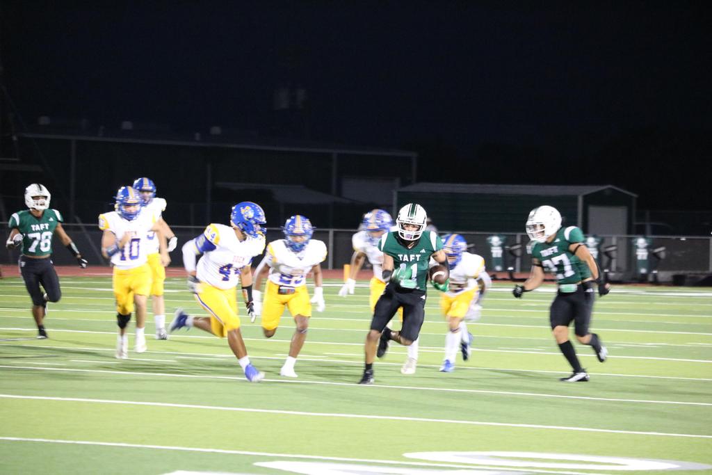 A football team sprinting across the field under the night sky, illuminated by stadium lights.
