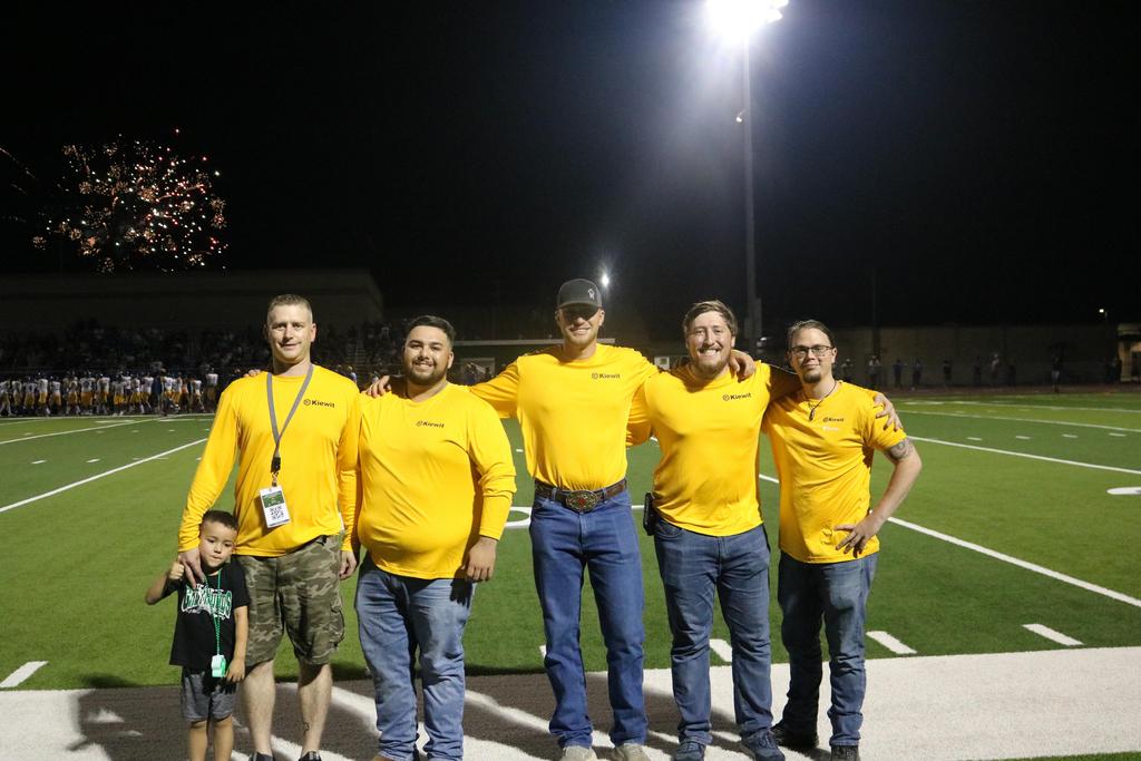A group of men wearing yellow shirts stands together on a football field, ready for a game or practice session.