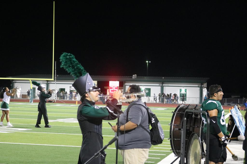 A band performs energetically on a field at night, illuminated by stage lights, creating a vibrant atmosphere.