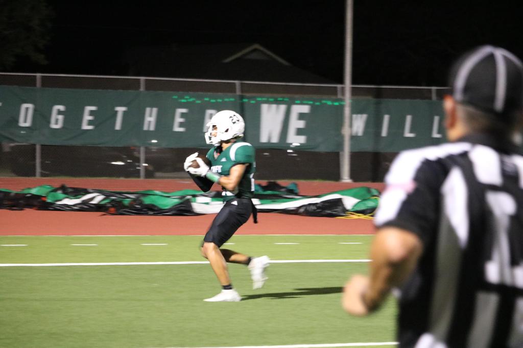 A football player sprinting down the field, skillfully carrying the ball as he navigates past defenders.