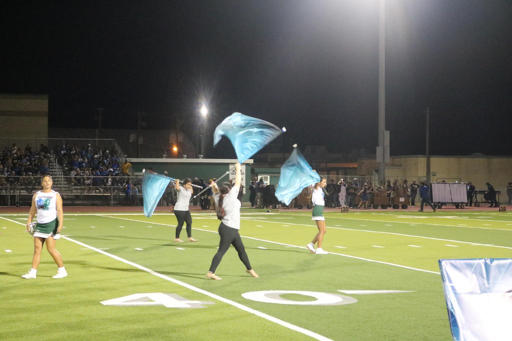 A cheerleading team performs on the field at night, illuminated by stadium lights, showcasing their vibrant uniforms and energy.