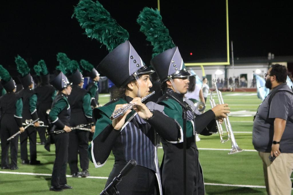 A vibrant marching band in green hats performs energetically at a lively football game, enhancing the festive atmosphere.