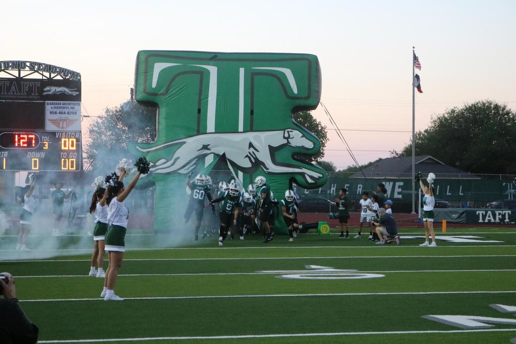 A football team stands on the field, surrounded by smoke billowing from the stadium in the background.