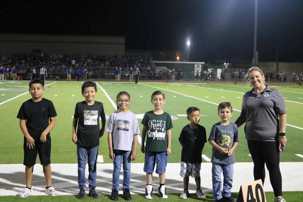 A group of children gathered on a football field, smiling and enjoying their time together in a sunny outdoor setting.