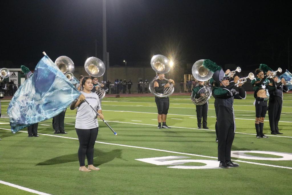 A band performing on a field at night, proudly displaying a flag under the illuminated sky.