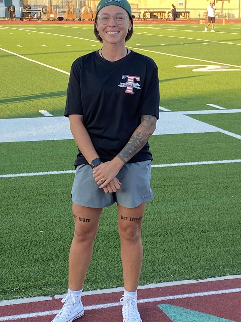 A woman with tattoos stands confidently on a vibrant soccer field, showcasing her unique style and passion for the sport.