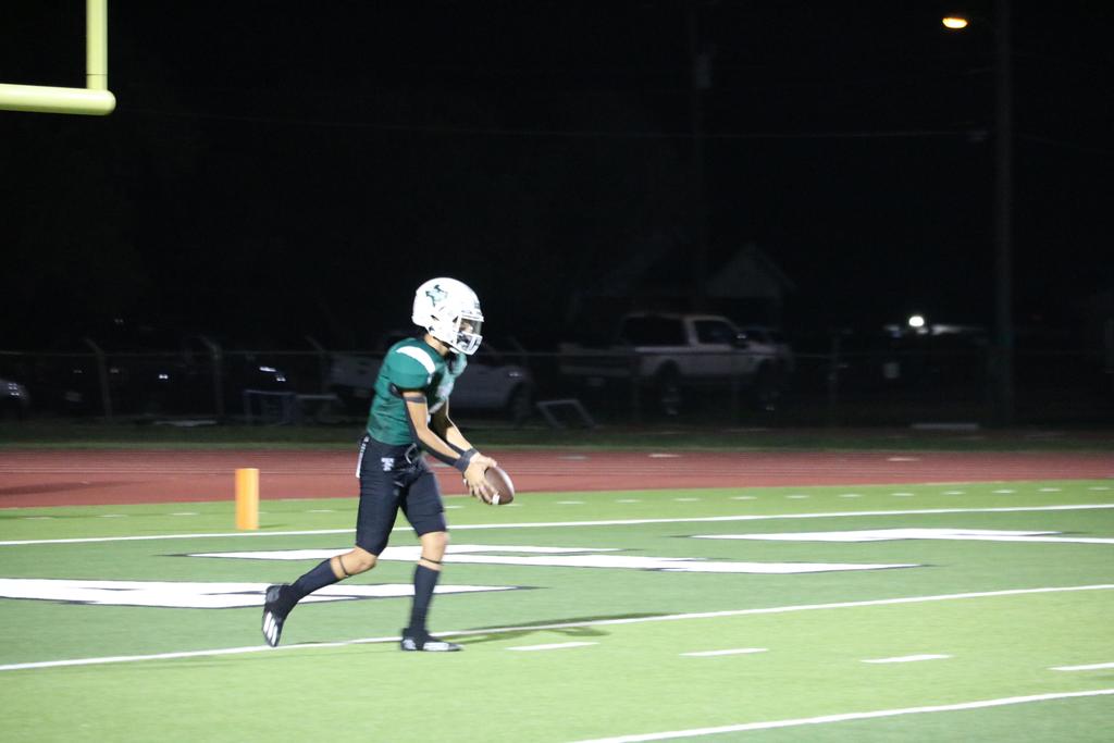 A football player sprinting across the field under the night sky, illuminated by stadium lights.