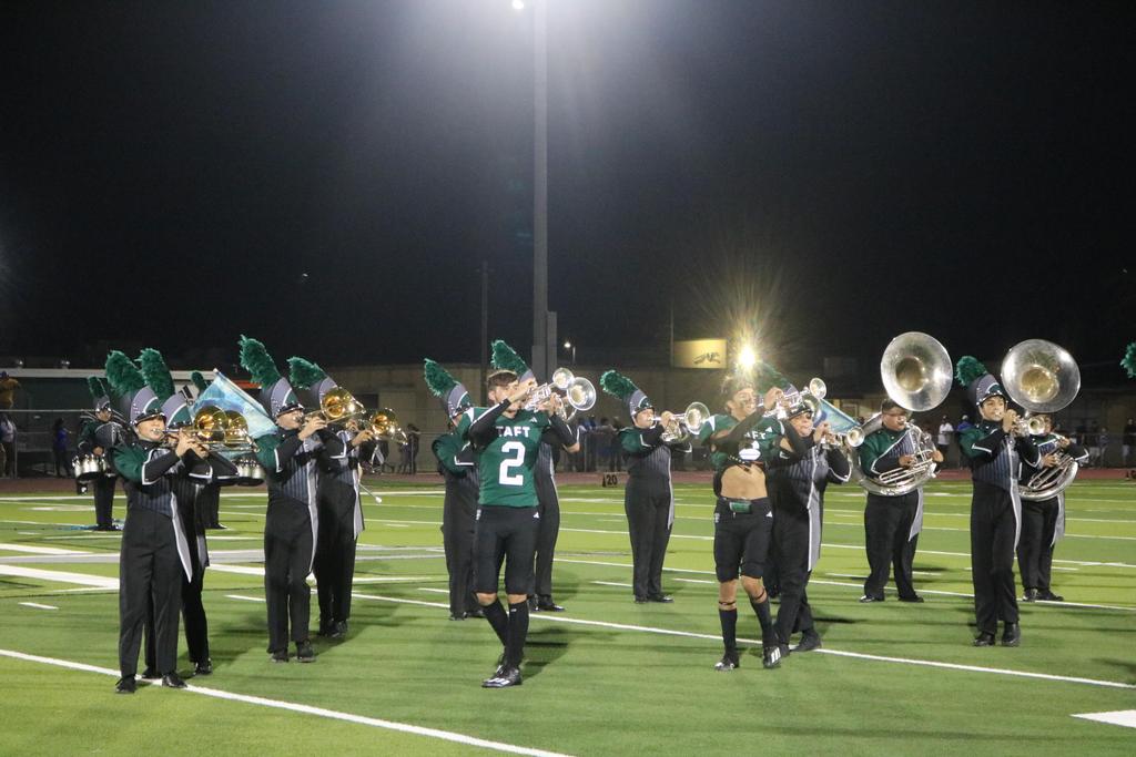 A vibrant marching band performs on a football field under the night sky, illuminated by stadium lights.