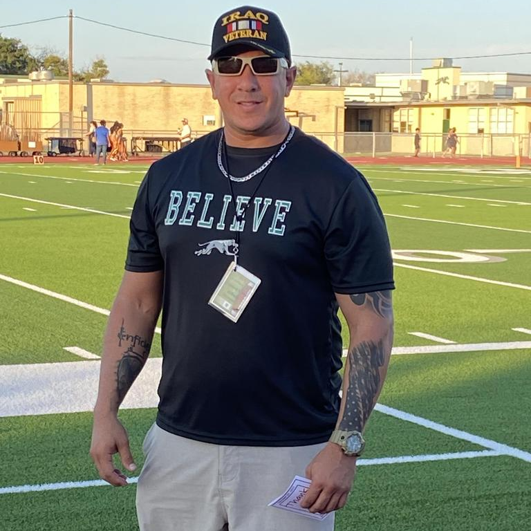 A man wearing a black shirt and shorts stands confidently on a football field, ready for action.