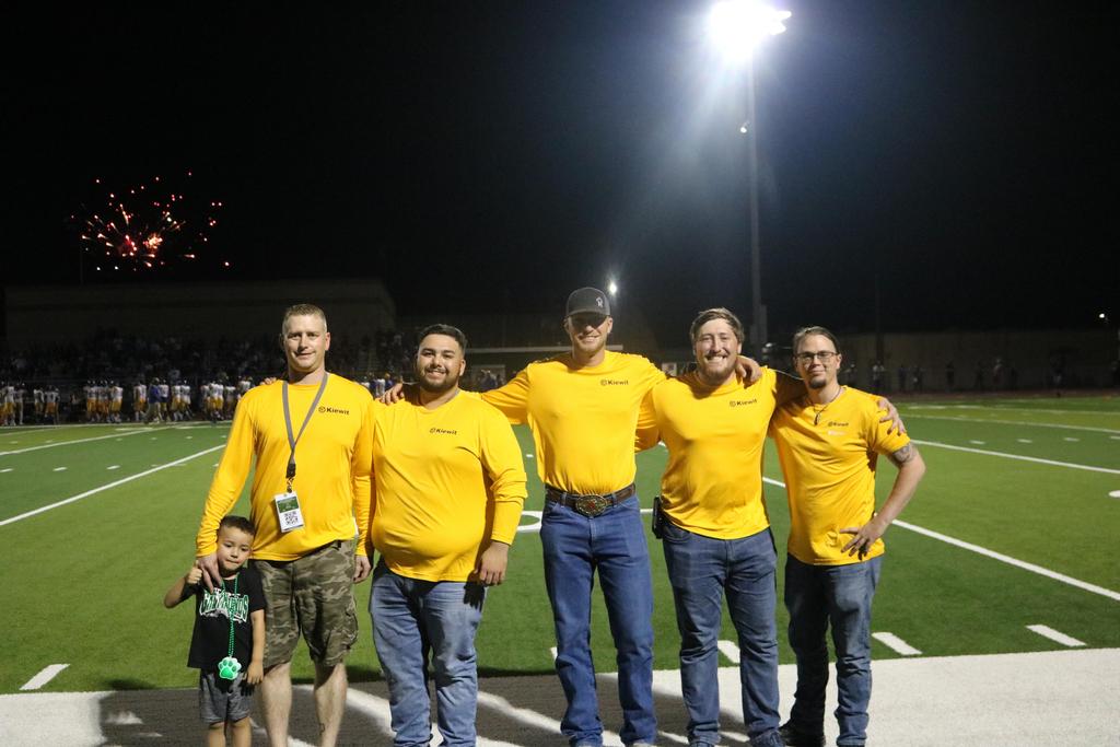 A group of men wearing yellow shirts stands together on a football field, ready for a game or practice session.