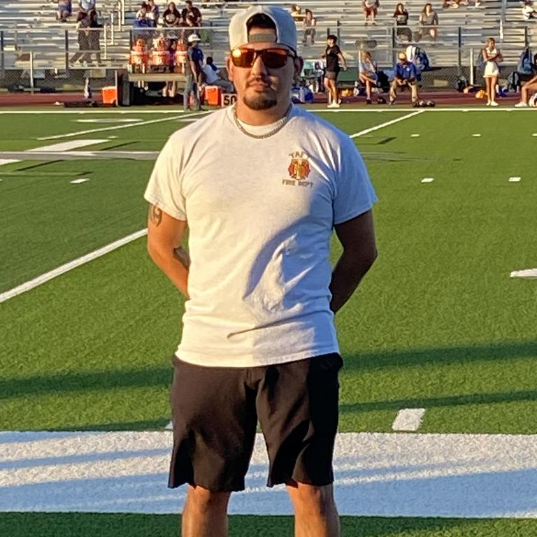A man wearing a white shirt and black shorts stands confidently on a football field, ready for action.