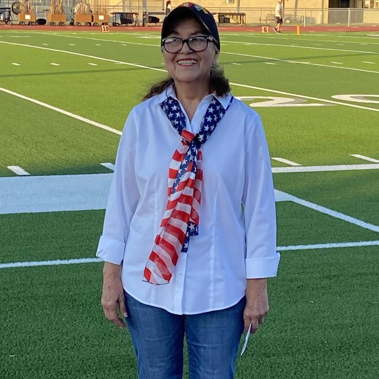 A woman proudly displays an American flag scarf while standing on a football field, showcasing her patriotic spirit.
