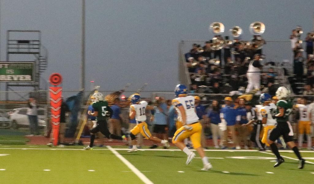 A lively football game in progress, featuring players in motion and a band performing in the background.