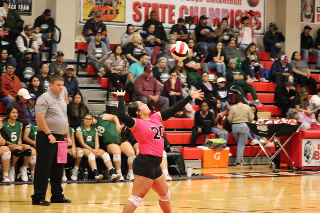 A girl wearing pink and black attire is actively playing volleyball on a sunny day.