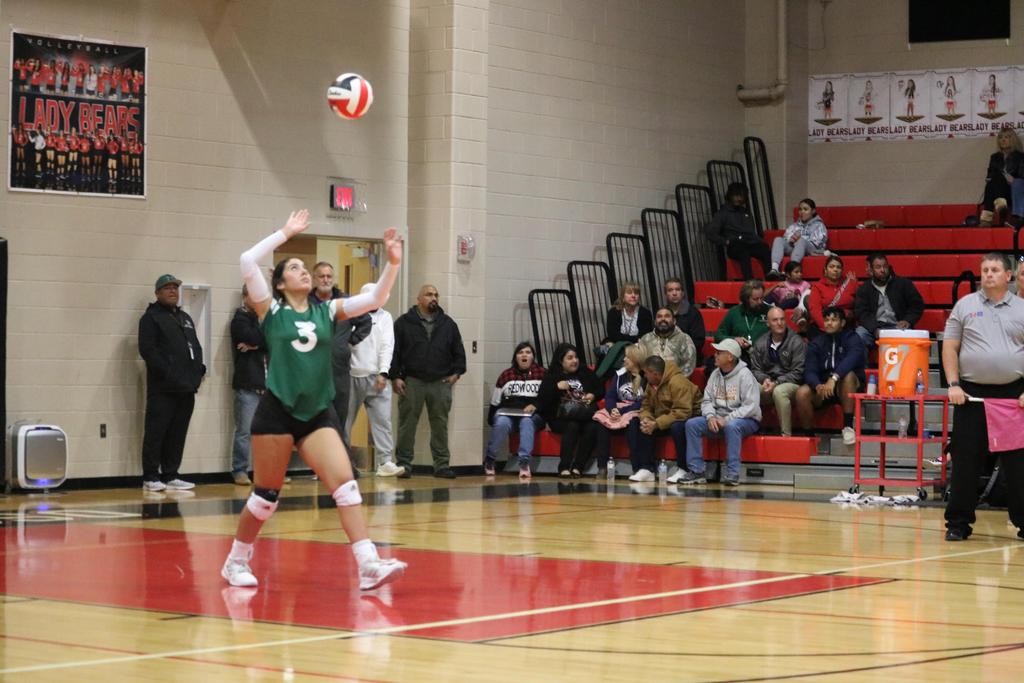 A girl in a green and white uniform skillfully playing volleyball on a sunny court.