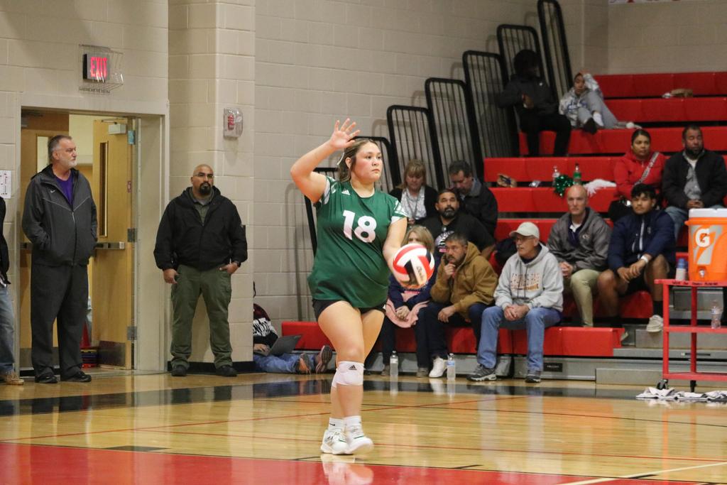 A girl in a green and white uniform is actively playing volleyball on a court, showcasing her athletic skills.