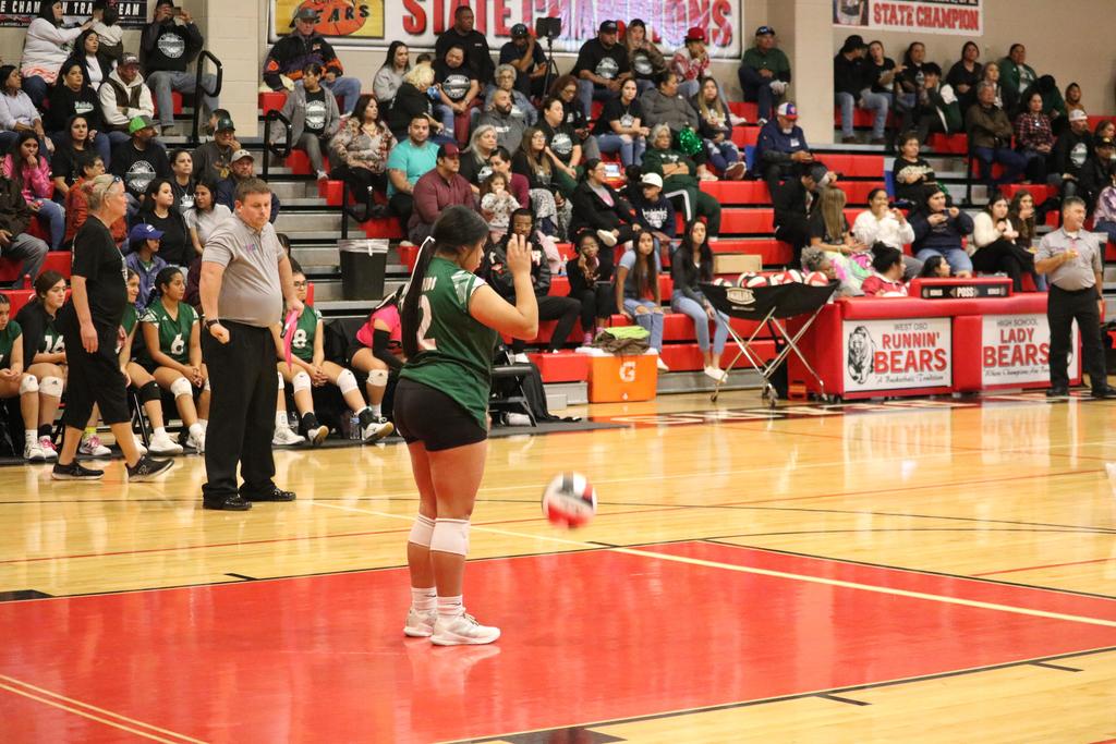 A girl in green and white attire skillfully playing volleyball on a sunny court.
