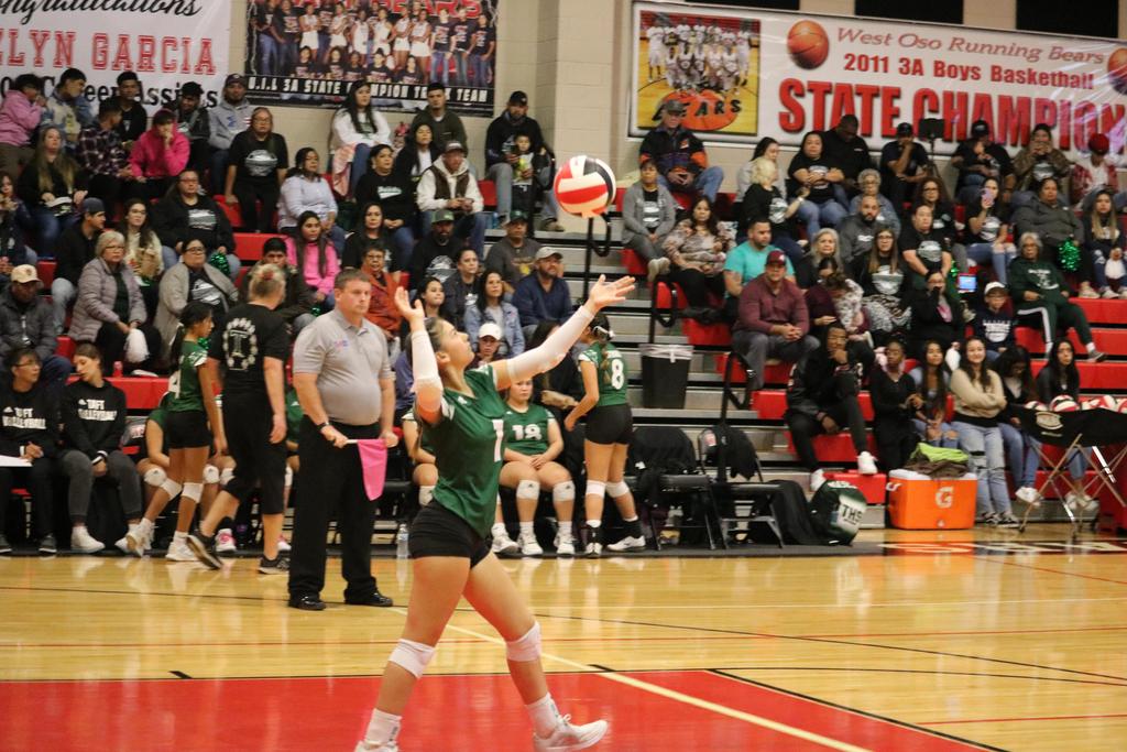 A girl in a green and white uniform skillfully playing volleyball on a sunny court.