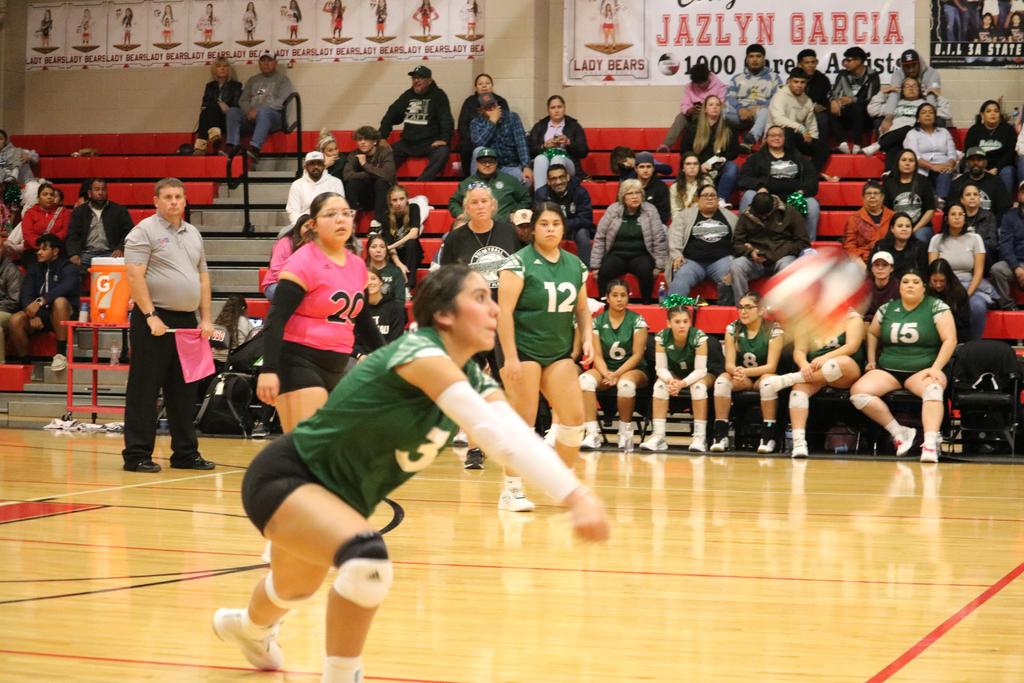 A girl in a green and white uniform skillfully playing volleyball on a sunny court.