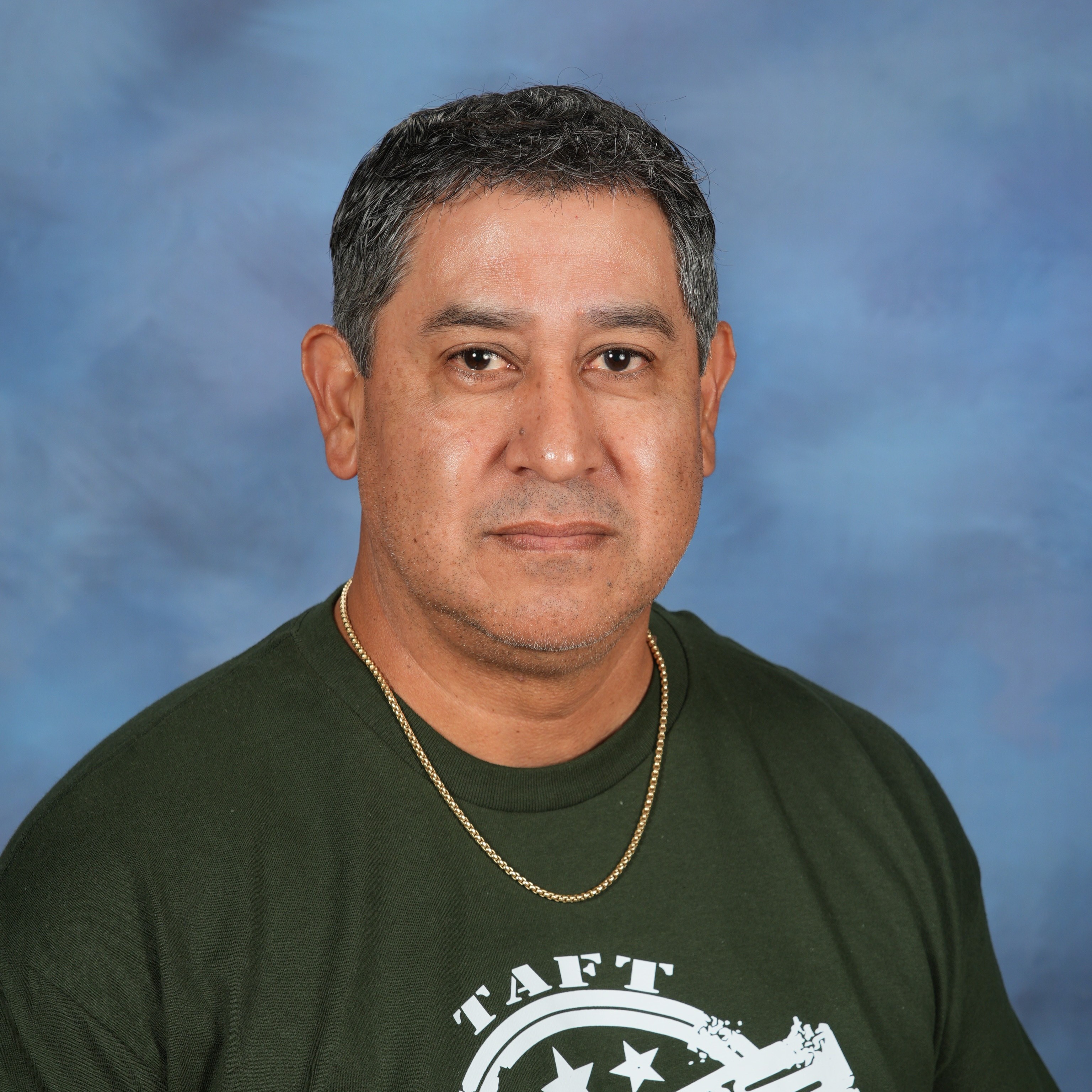 A man wearing a green shirt stands against a solid blue background.