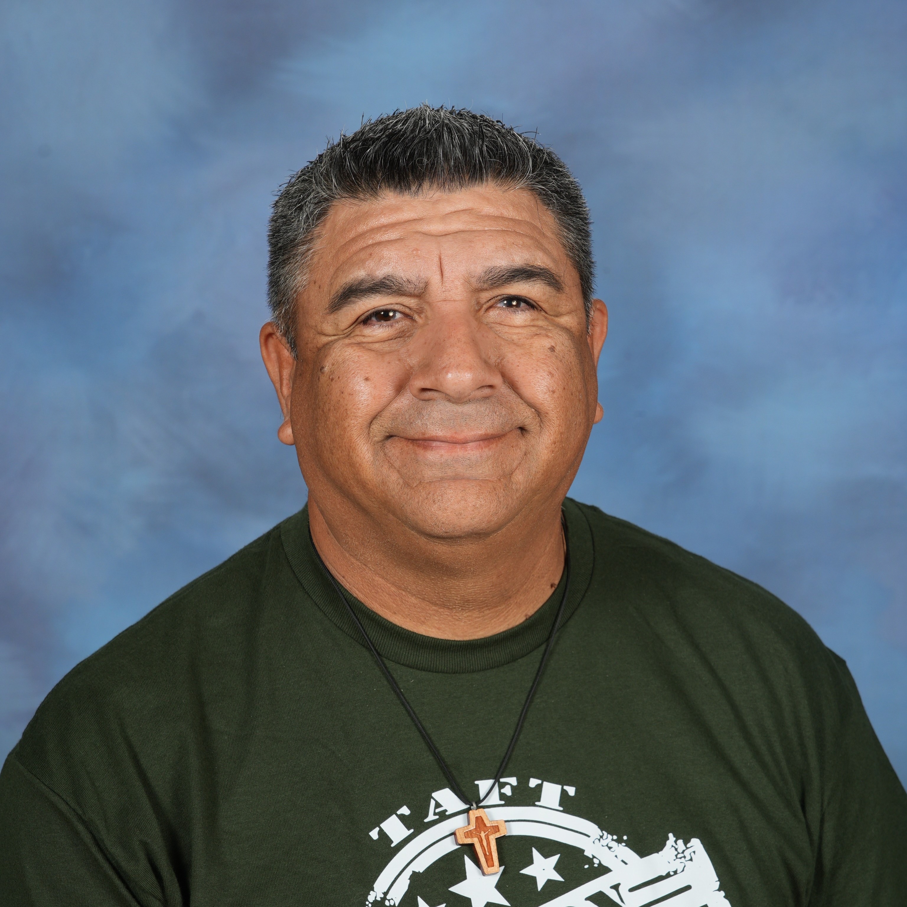 A man wearing a green polo shirt stands confidently against a solid blue background.