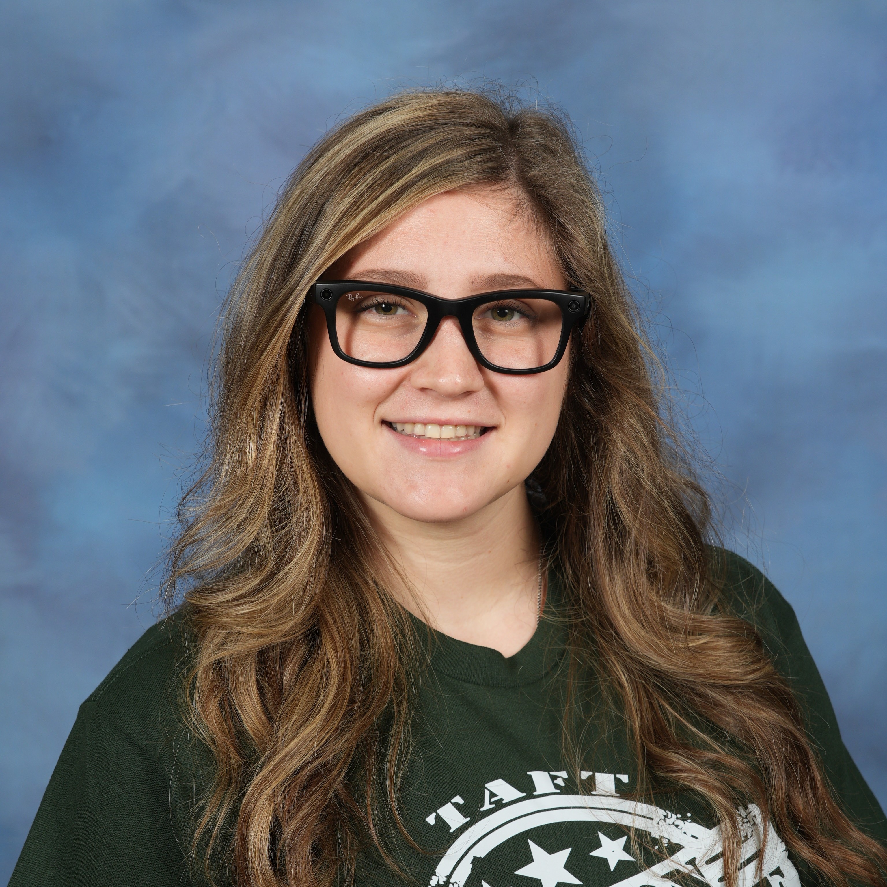A woman with glasses wearing a green shirt, smiling and looking confidently at the camera.