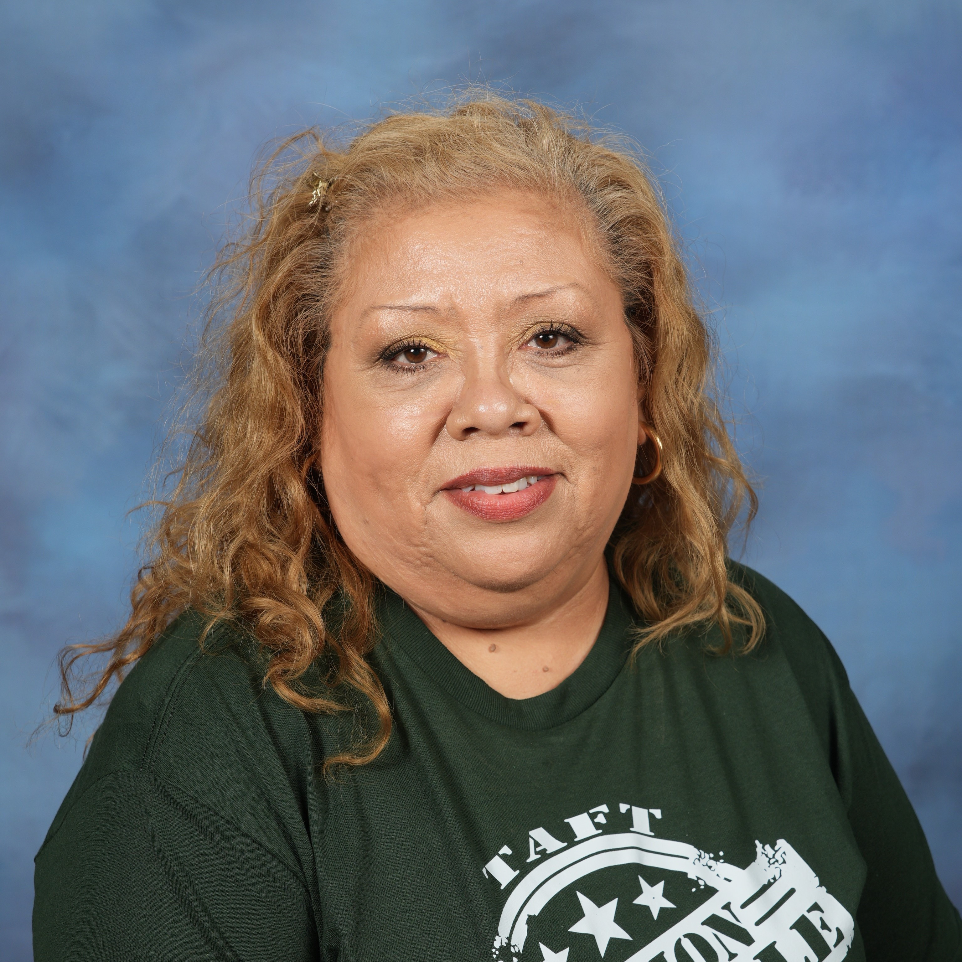 A woman wearing a green shirt and jeans stands confidently, showcasing a casual yet stylish outfit.