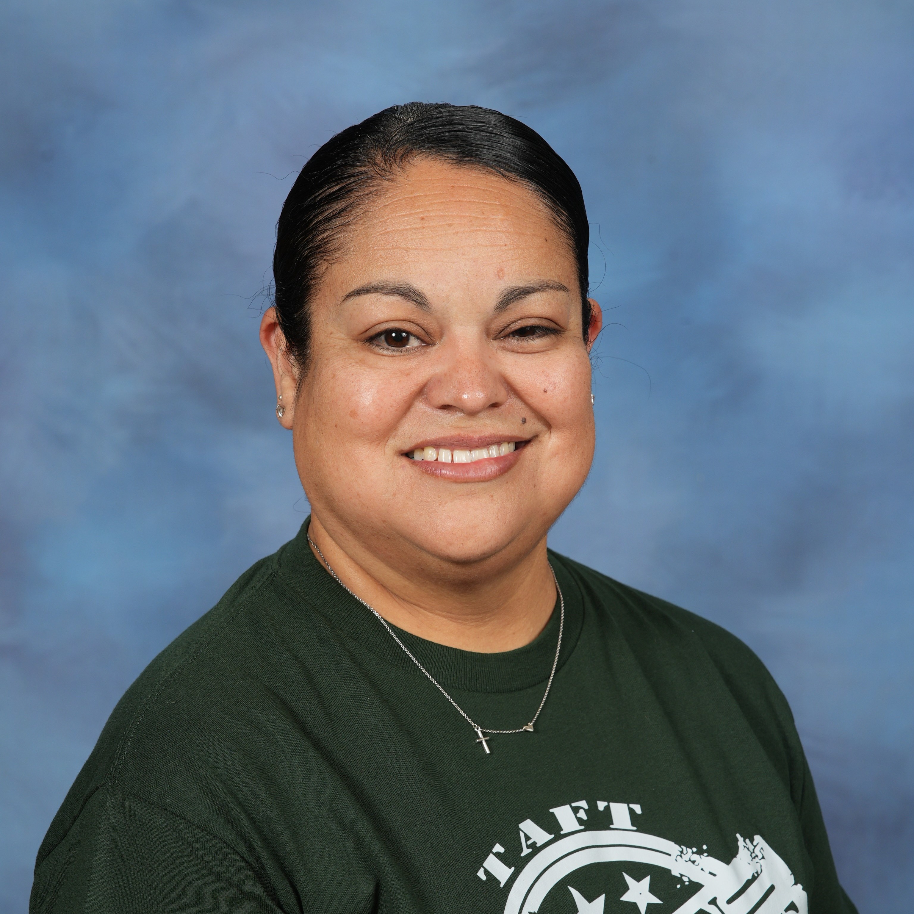 A woman wearing a green shirt and glasses stands against a blue background.